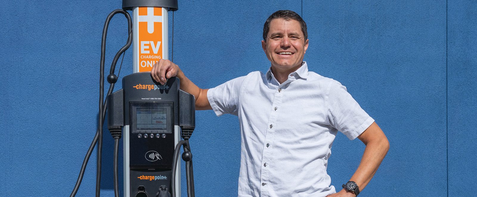 Alum Doug Campbell smiling and posing with electric vehicle charging station