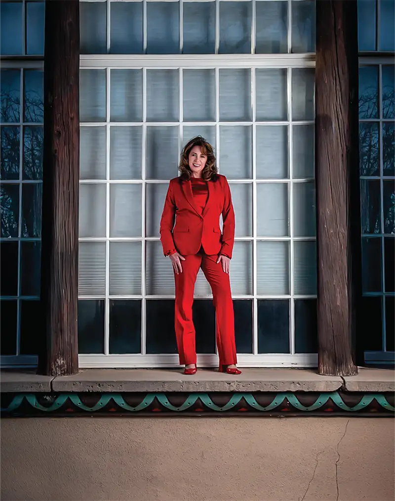 Aprilyn Chavez Geissler standing in a red suit in front of a large window