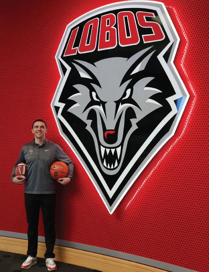 Ryan Berryman standing in front of an illuminated Lobos logo on the wall